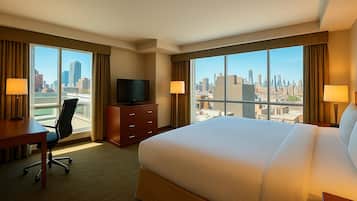 A hotel room with a large bed, a desk with a chair, a television, and a view of the city skyline.