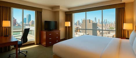 A hotel room with a large bed, a desk with a chair, a television, and a view of the city skyline.