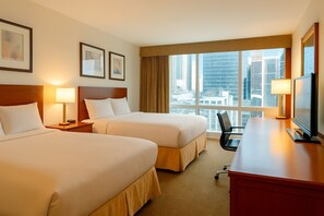 A hotel room with two beds, a desk, a chair, and a large window offering a city view. - LIC Manhattan View Hotel (Long Island City)