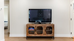 Een flatscreen televisie op een houten kast met glazen deuren, een witte muur en een houten vloer.