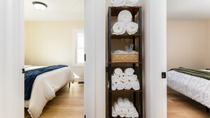Een hotelkamer met twee bedden, een houten vloer, een plank met netjes opgevouwen handdoeken en een mandje met toiletartikelen.
