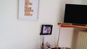 Een eethoek met een tafel gedekt voor twee personen, een televisie op een standaard en een ingelijste quote aan de muur.