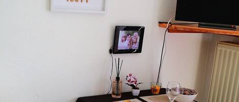 A dining area with a table set for two, a television on a stand, and a framed quote on the wall.