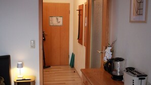 Een hotelkamer met een houten vloer, een houten dressoir, een klein tafeltje met een lamp, een bed en een ingelijst schilderij aan de muur.