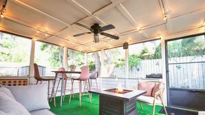 Un patio couvert avec un ventilateur de plafond, un foyer extérieur, une pelouse artificielle et des meubles d’extérieur.