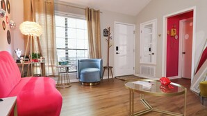 Un salon avec un canapé rouge, un fauteuil bleu, une table basse en verre et un plancher en bois.