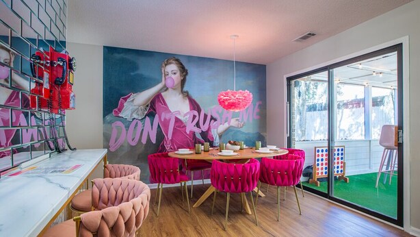Un espace de restauration moderne agrémenté d’une fresque murale, de chaises roses et d’une table en verre.