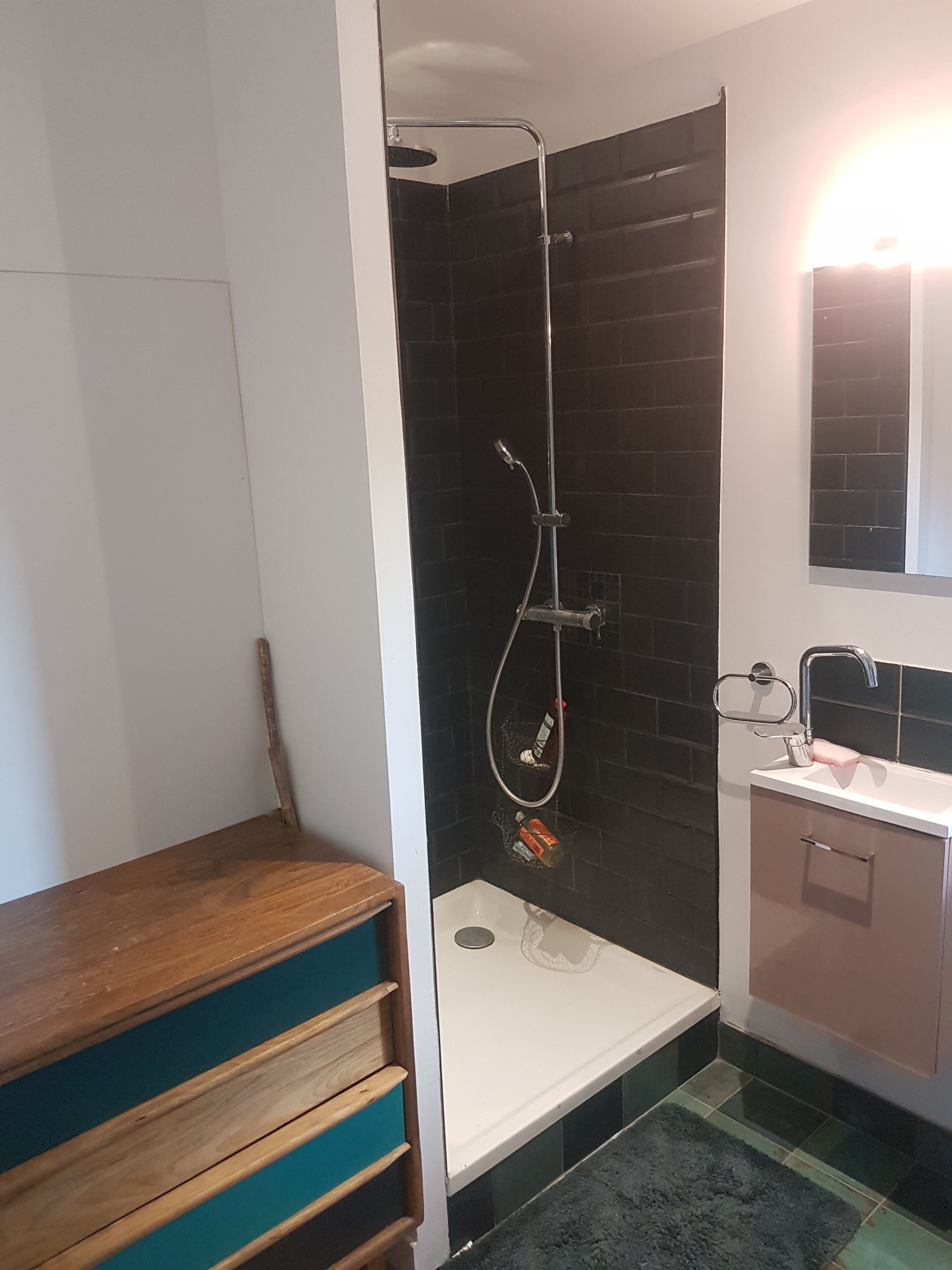 Une salle de bain moderne avec une douche à parois de verre, un lavabo blanc et un banc en bois.