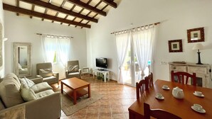 Ein Wohnzimmer mit einer Couch, Sesseln, einem Couchtisch, einem Fernseher und einem Essbereich mit Tisch und Stühlen.