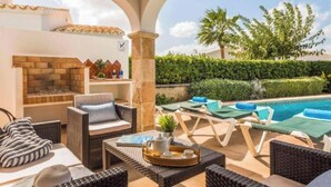 Eine Terrasse im Freien mit Korbmöbeln, Grillplatz und Pool.