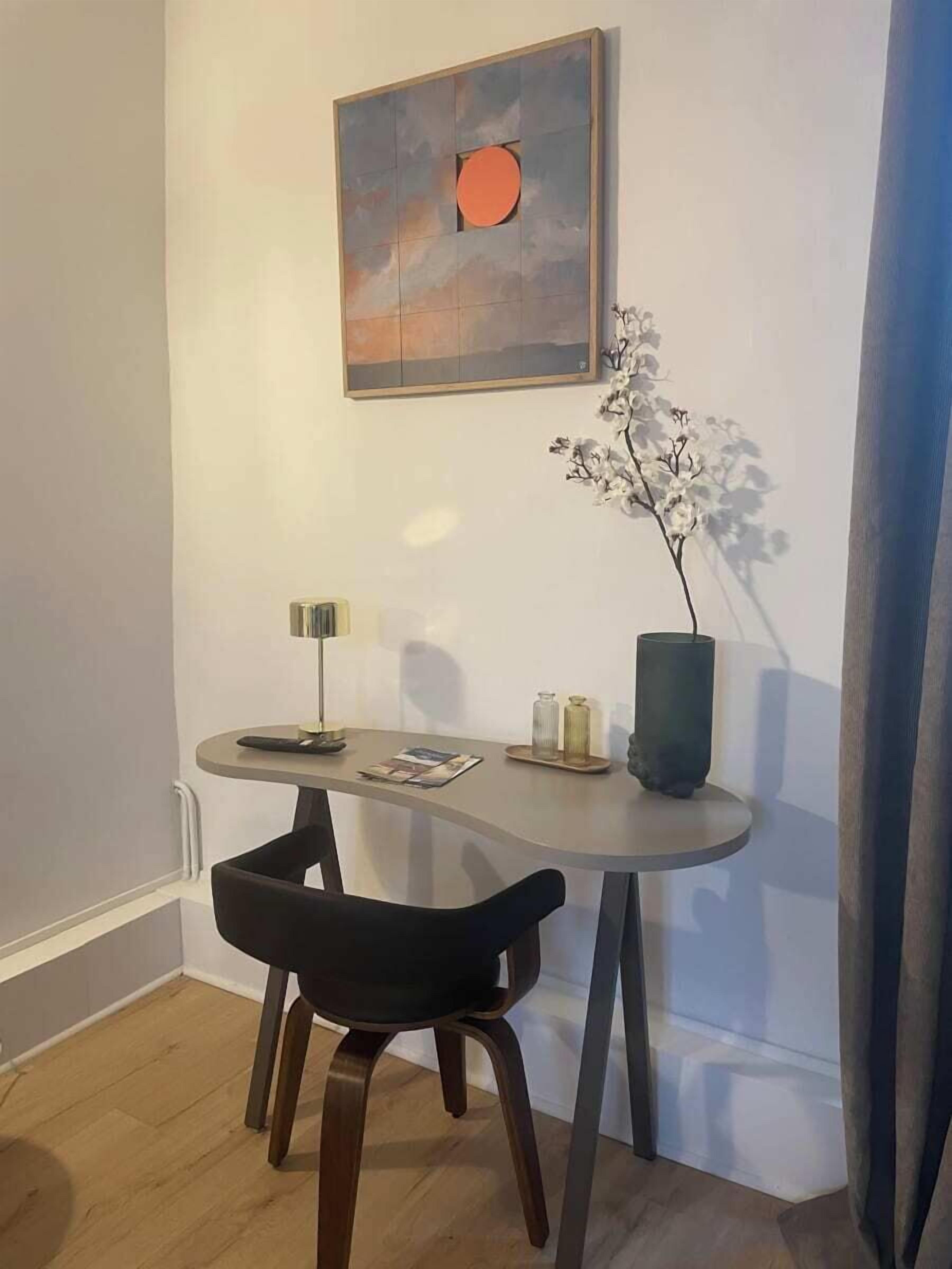 A small dining area with a table, two chairs, a vase with flowers, and a painting on the wall.