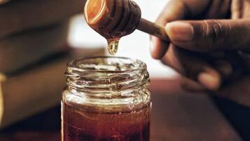 A hand holding a honey dipper dripping honey into a jar.