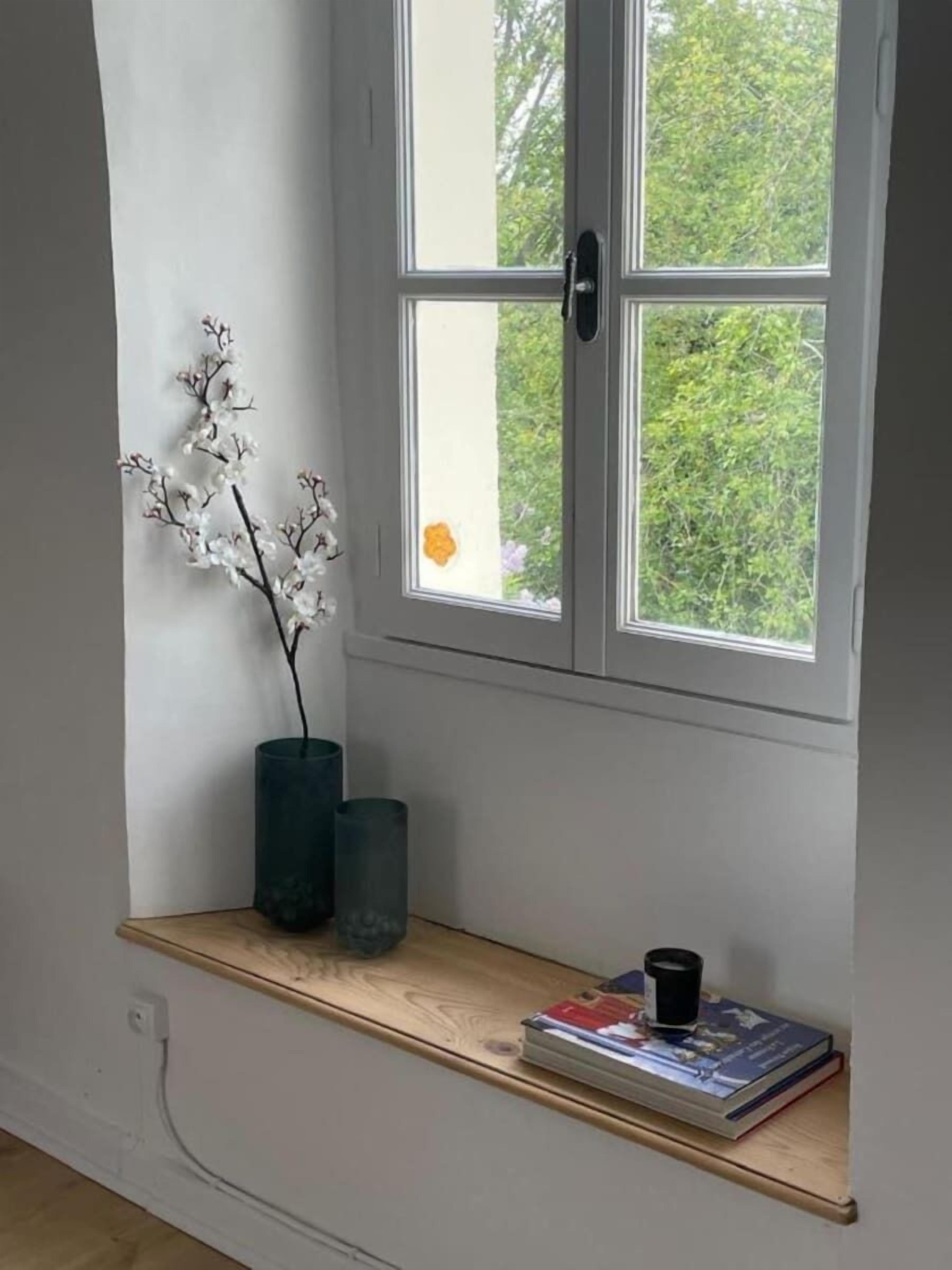 Een kamer met een raam, een houten plank, een vaas met bloemen en een boek.