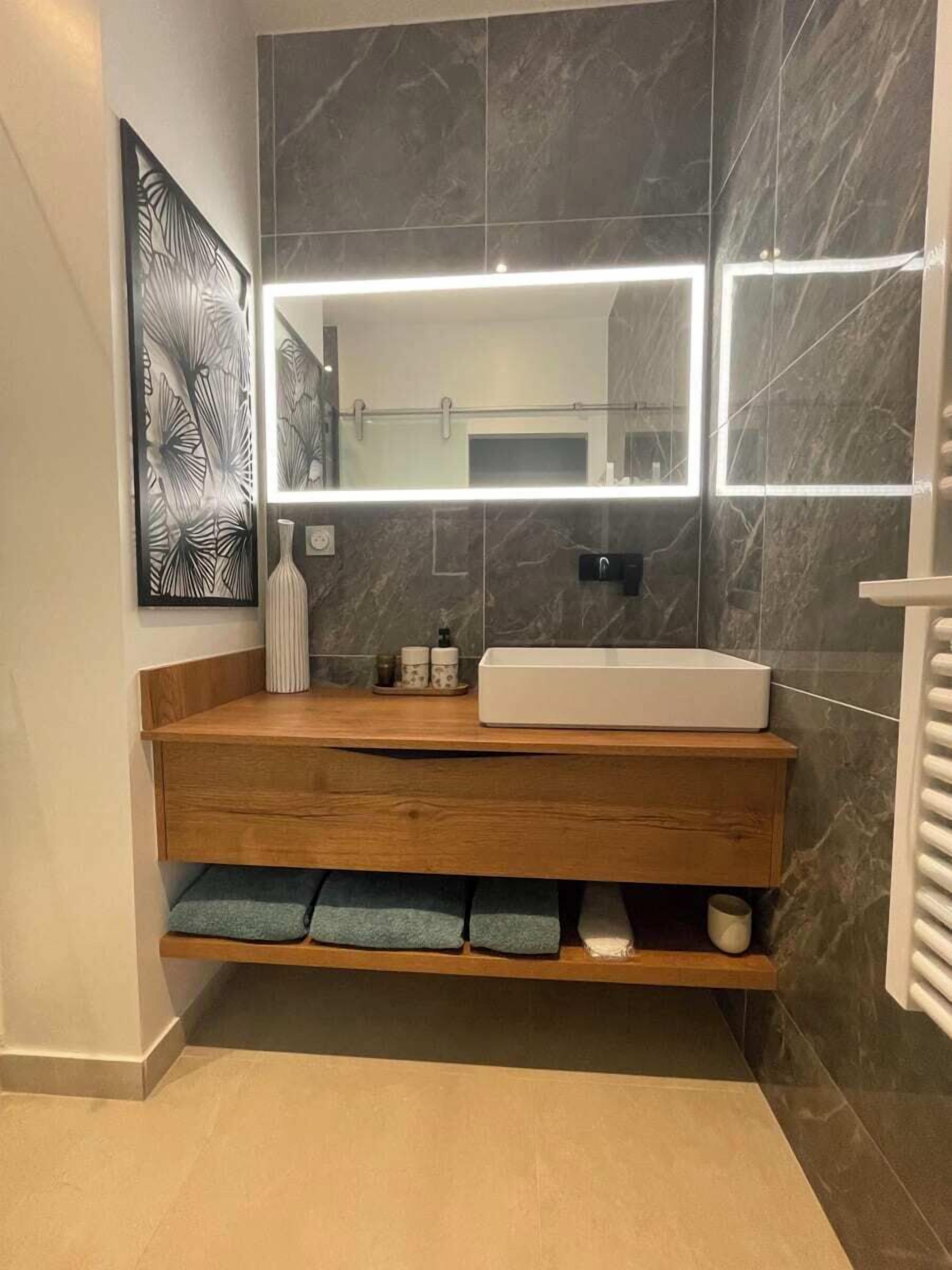 Een moderne badkamer met een houten wastafelmeubel, een grote spiegel en een marmeren achterwand.