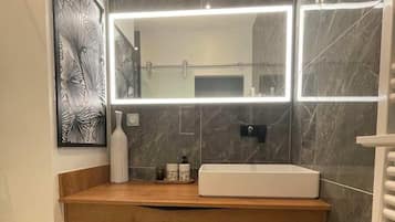 Un baño moderno con tocador de madera, un espejo grande y un salpicadero de mármol.