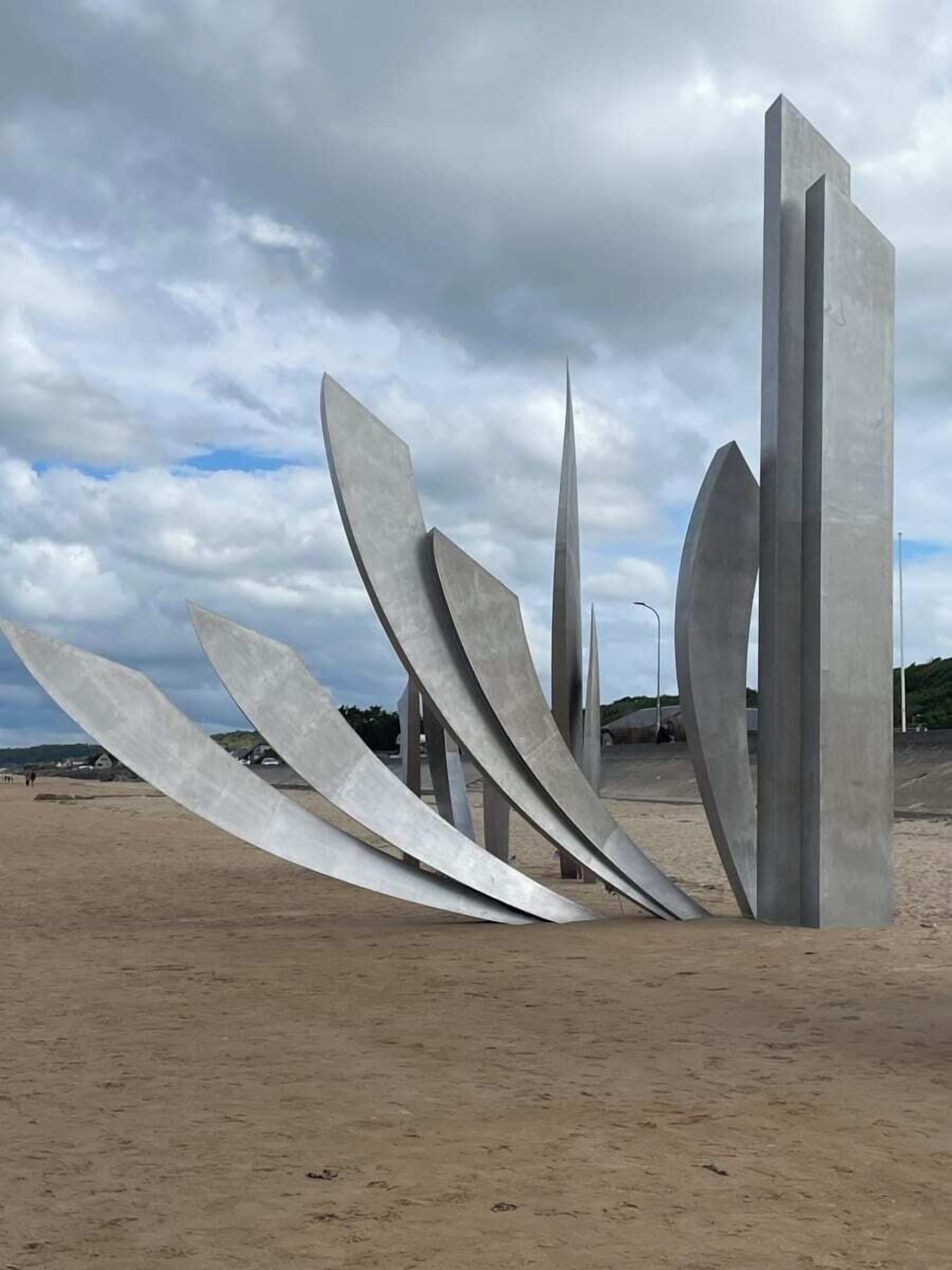 Escultura moderna com formas geométricas numa praia arenosa.