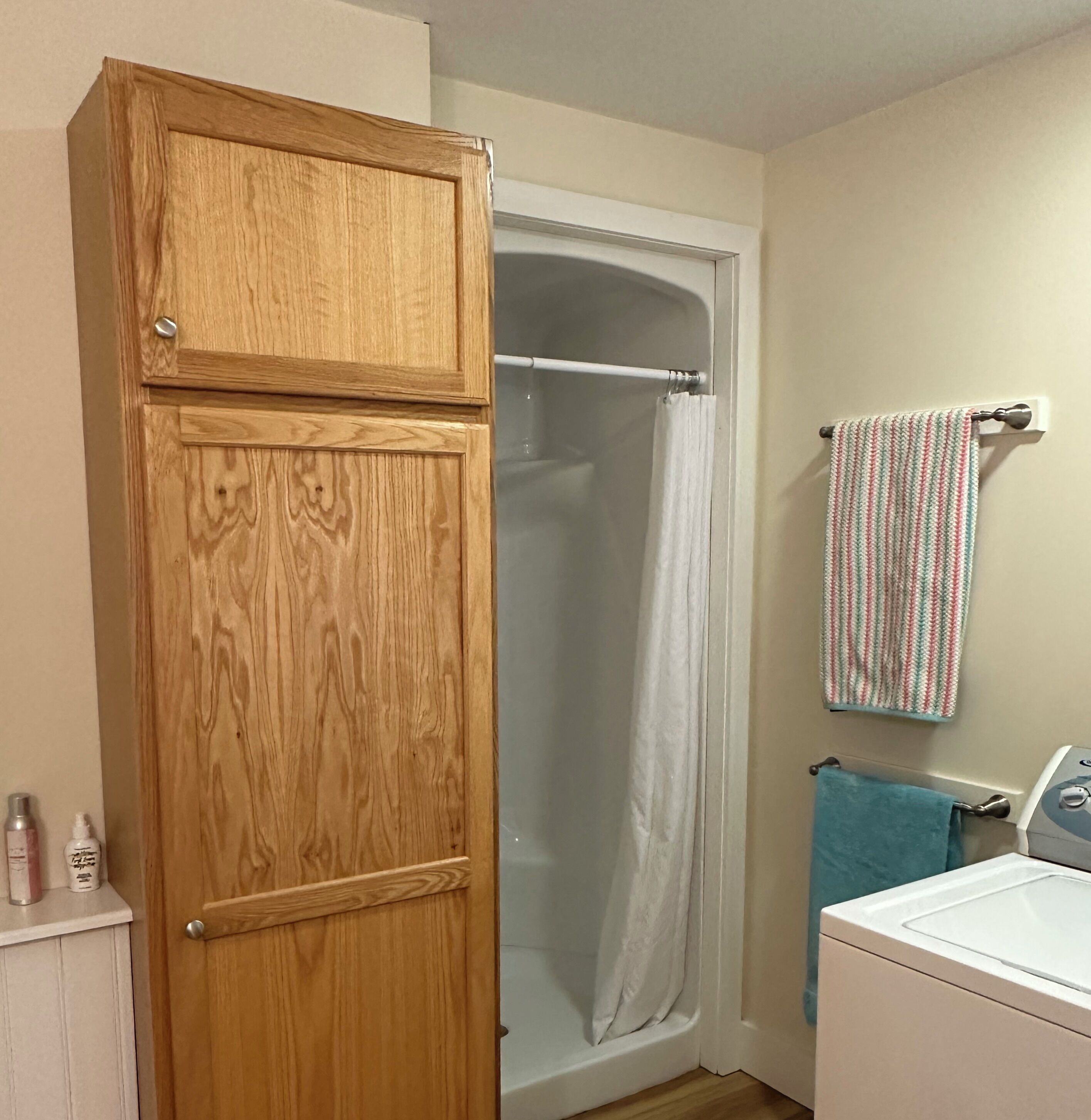 A bathroom with a wooden cabinet, a shower curtain, a towel rack with a striped towel, and a washing machine.