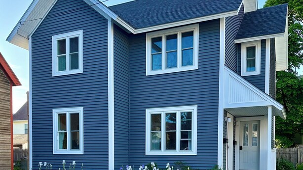 A two-story house with a front porch, multiple windows, and a well-maintained garden with flowers and shrubs. -  In-Town Bar Harbor, One Bedroom, Huckleberry Suit (Bar Harbor)