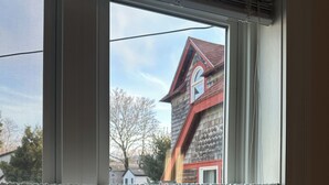 A window with white curtains, a view of a house with a red roof, and a clear sky. -  In-Town Bar Harbor, One Bedroom, Huckleberry Suit (Bar Harbor)