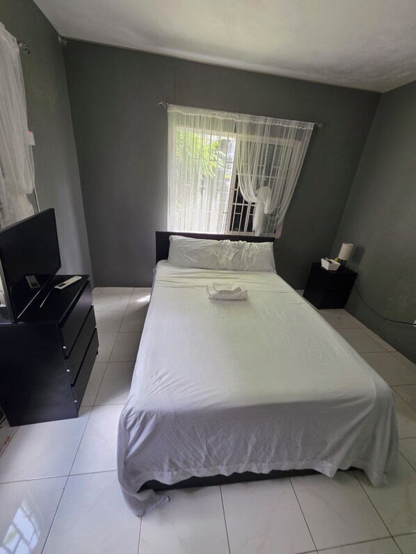 A bedroom with a bed, a dresser, a bedside table, and a window with curtains.