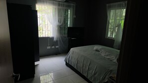 Quarto com iluminação suave, uma cama, televisão e janela com cortinas finas.
