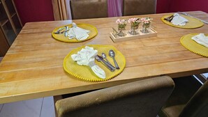 Una mesa de comedor de madera con individuales amarillos, cuidadosamente dispuesta con servilletas blancas, cubiertos y un centro de mesa con pequeños jarrones de vidrio con flores.