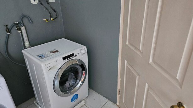 A front-loading washing machine in a small laundry room with a door and a wall-mounted electrical outlet. - Relax & Unwind in Our Tranquil Space at Jamaica b&b rentals (Montego Bay)