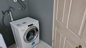 A front-loading washing machine in a small laundry room with a door and a wall-mounted electrical outlet.