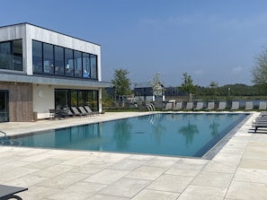Um edifício moderno com piscina, espreguiçadeiras e céu azul.