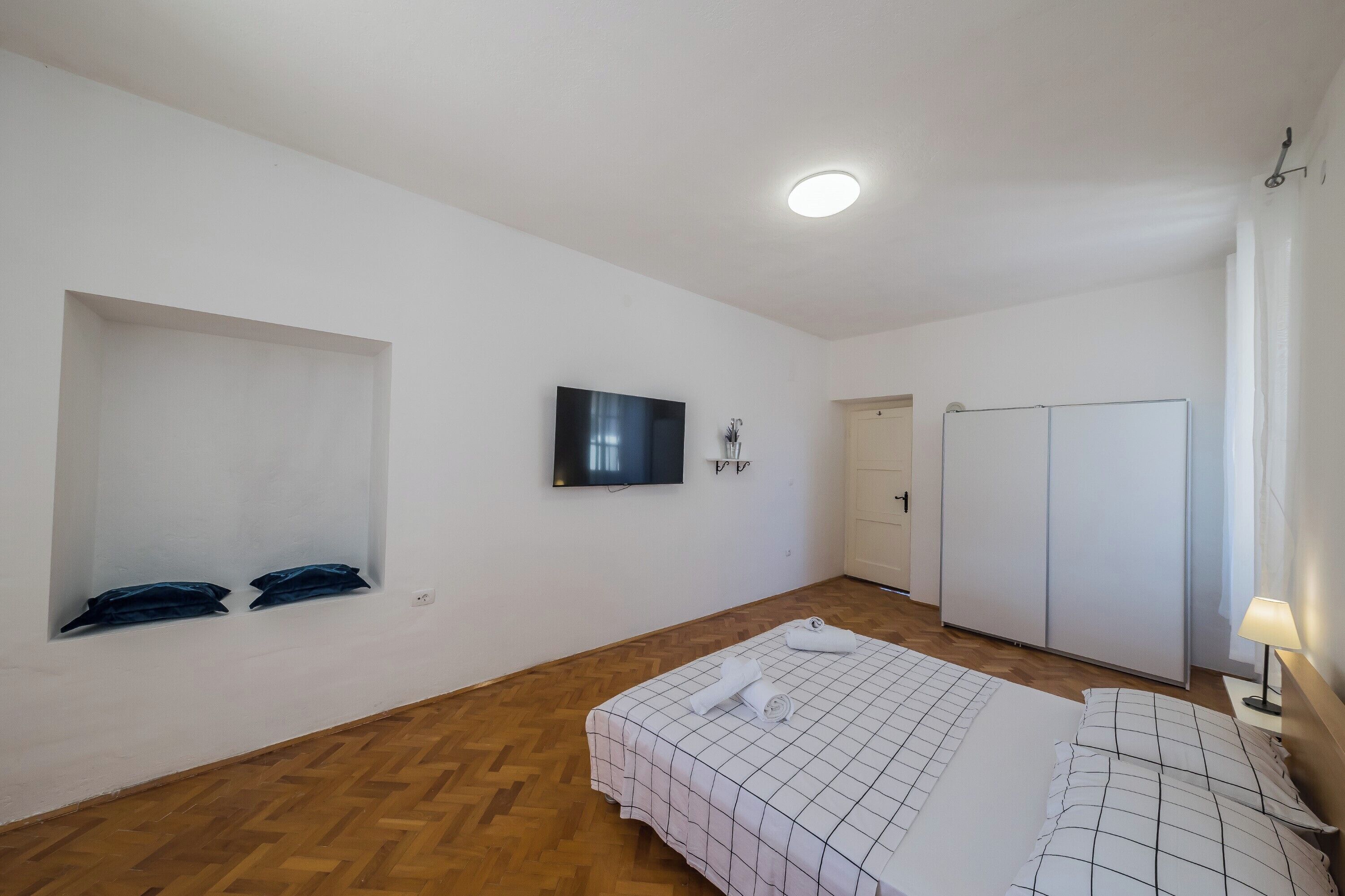 Un dormitorio con cama, televisión, armario y ventana con maletas.