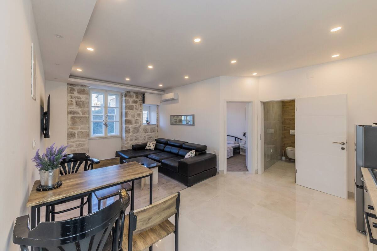 Una sala de estar moderna con un sofá de cuero negro, una mesa de comedor de madera y una pared de acento de piedra.