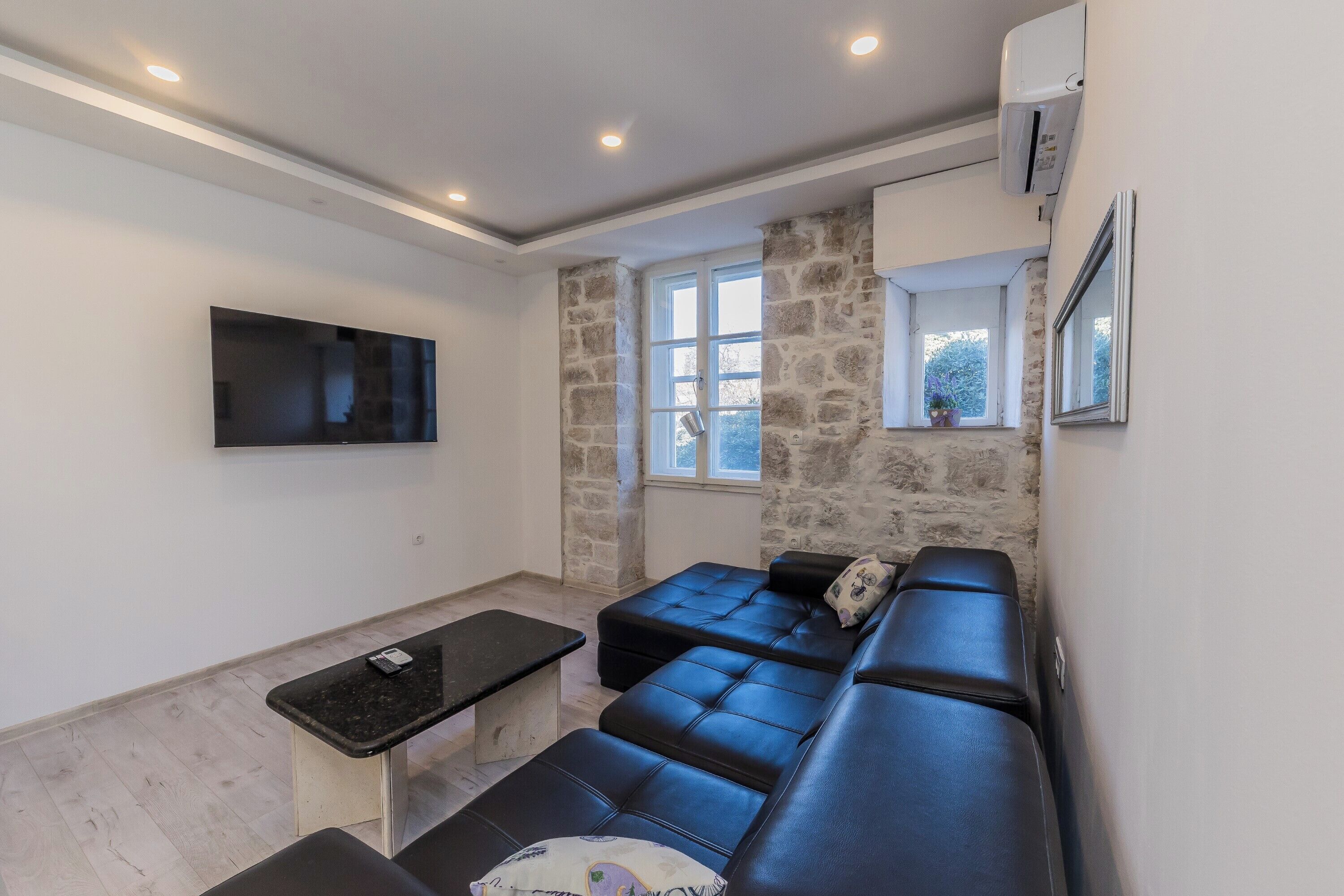 Un salón moderno con un sofá de cuero negro, una mesita pequeña negra y un televisor montado en la pared.