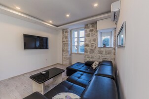 Un salón moderno con un sofá de cuero negro, una mesita pequeña negra y un televisor montado en la pared.