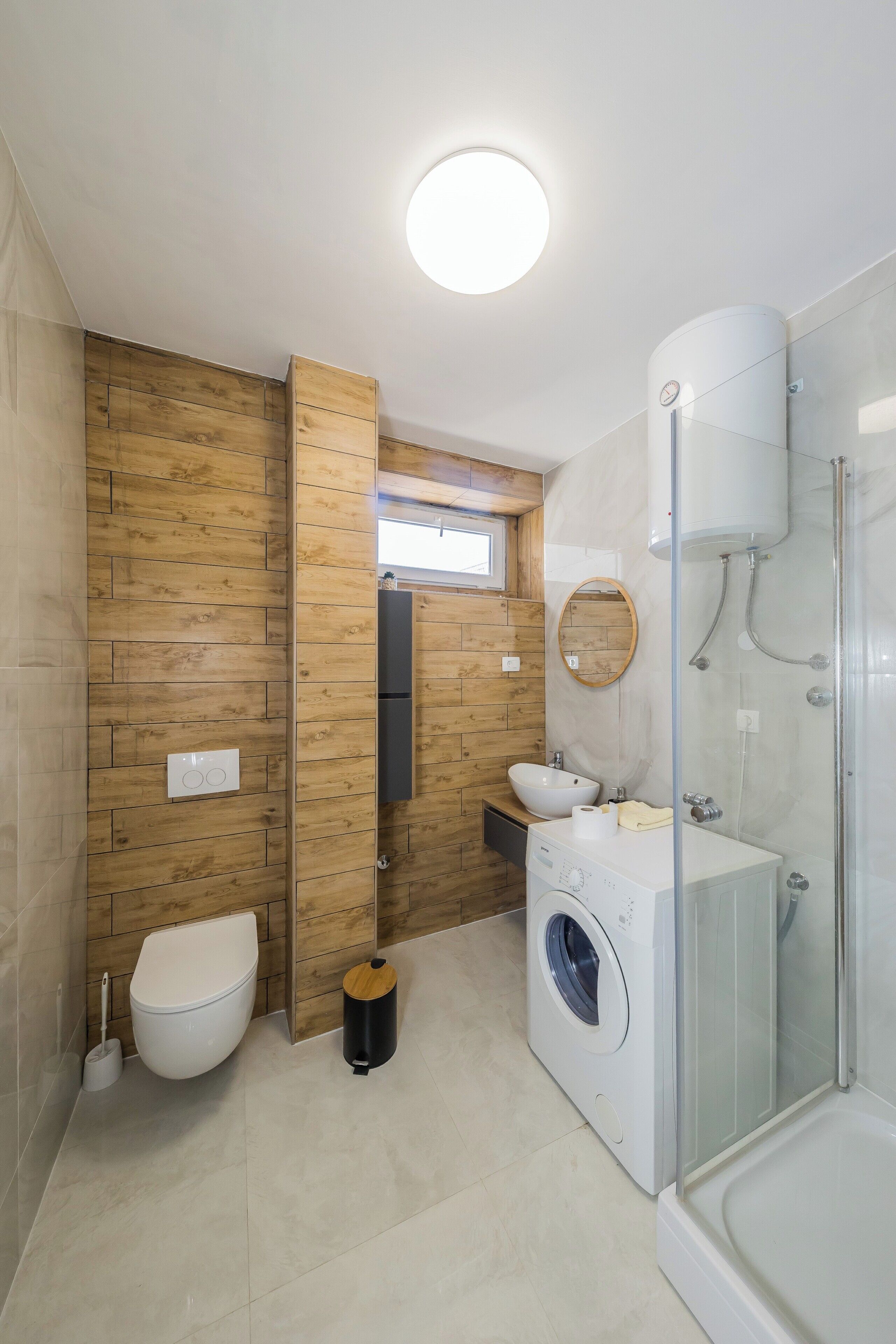 Une salle de bain moderne avec un mur en bois, des toilettes, un lave-linge, un évier et une douche à parois de verre.