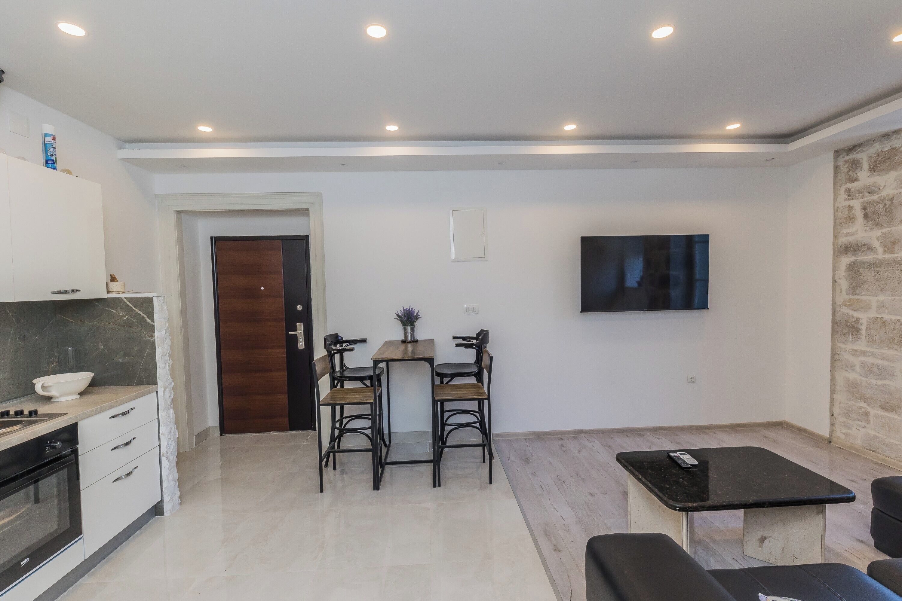 Una cocina moderna con armarios blancos, horno empotrado y comedor con mesa y sillas de madera.