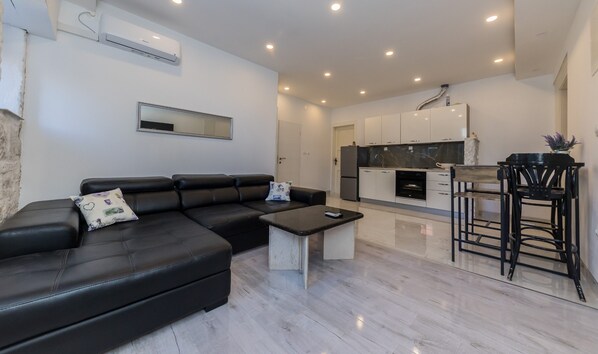 A modern living room with a black leather sofa, a small coffee table, and a kitchen area with white cabinets and a black countertop.