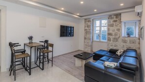 Ein modernes Wohnzimmer mit einem schwarzen Ledersofa, einem Holzesstisch mit Stühlen, einem an der Wand befestigten Fernseher und einer Steinwand.