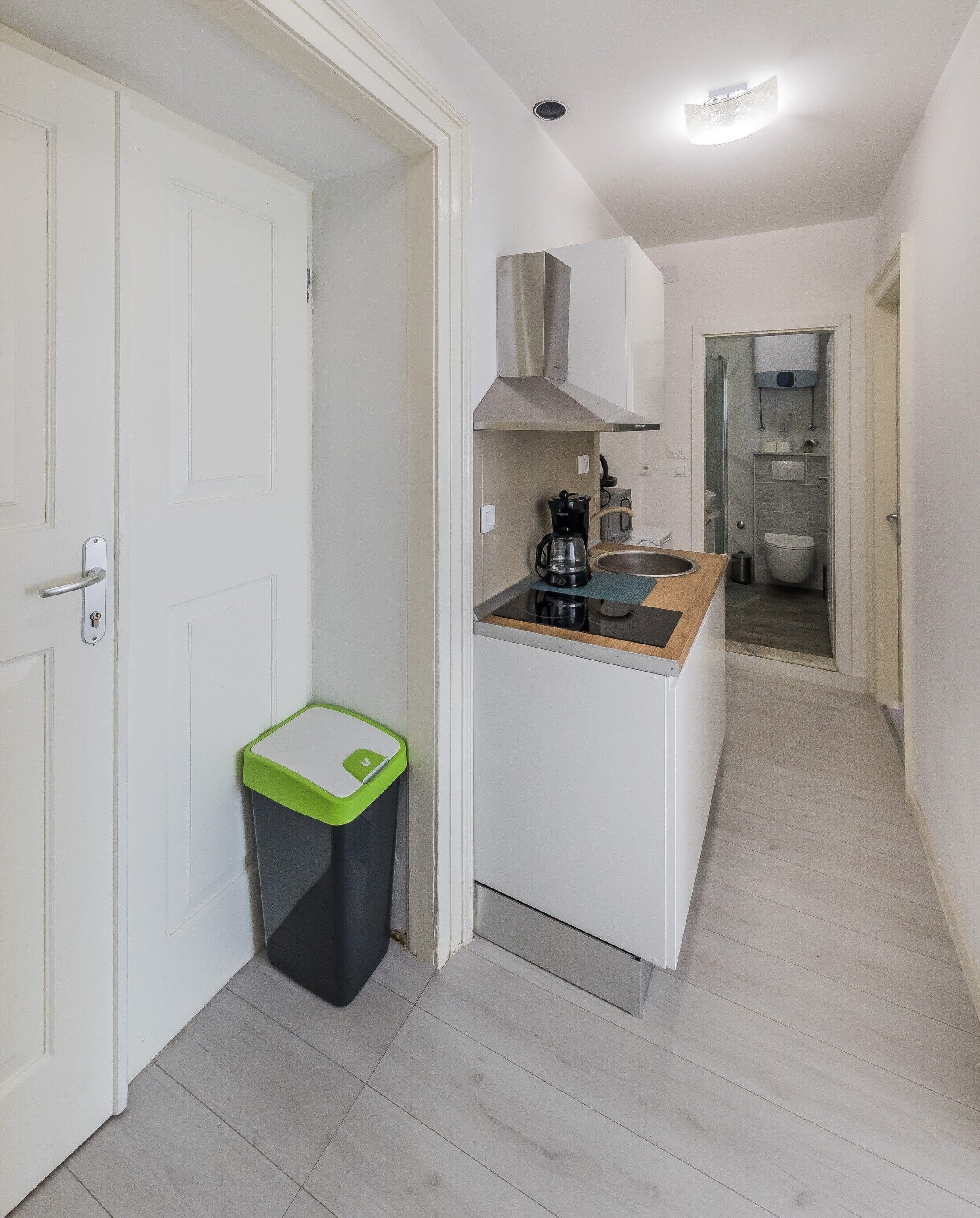 A compact kitchen with a coffee maker, a trash bin, and a sink.