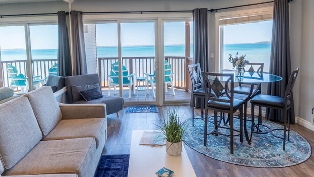 Ein Wohnzimmer mit Sofa, Couchtisch und Esstisch mit Stühlen. Durch große Fenster ist der Meerblick zu sehen.