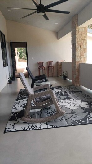 Una habitación amplia con ventilador de techo, alfombra estampada y dos sillas de madera.