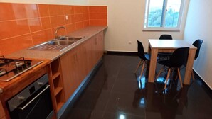 Une cuisine compacte équipée d’une cuisinière à gaz, d’un four et d’un évier, de placards en bois et d’une table à manger avec des chaises.