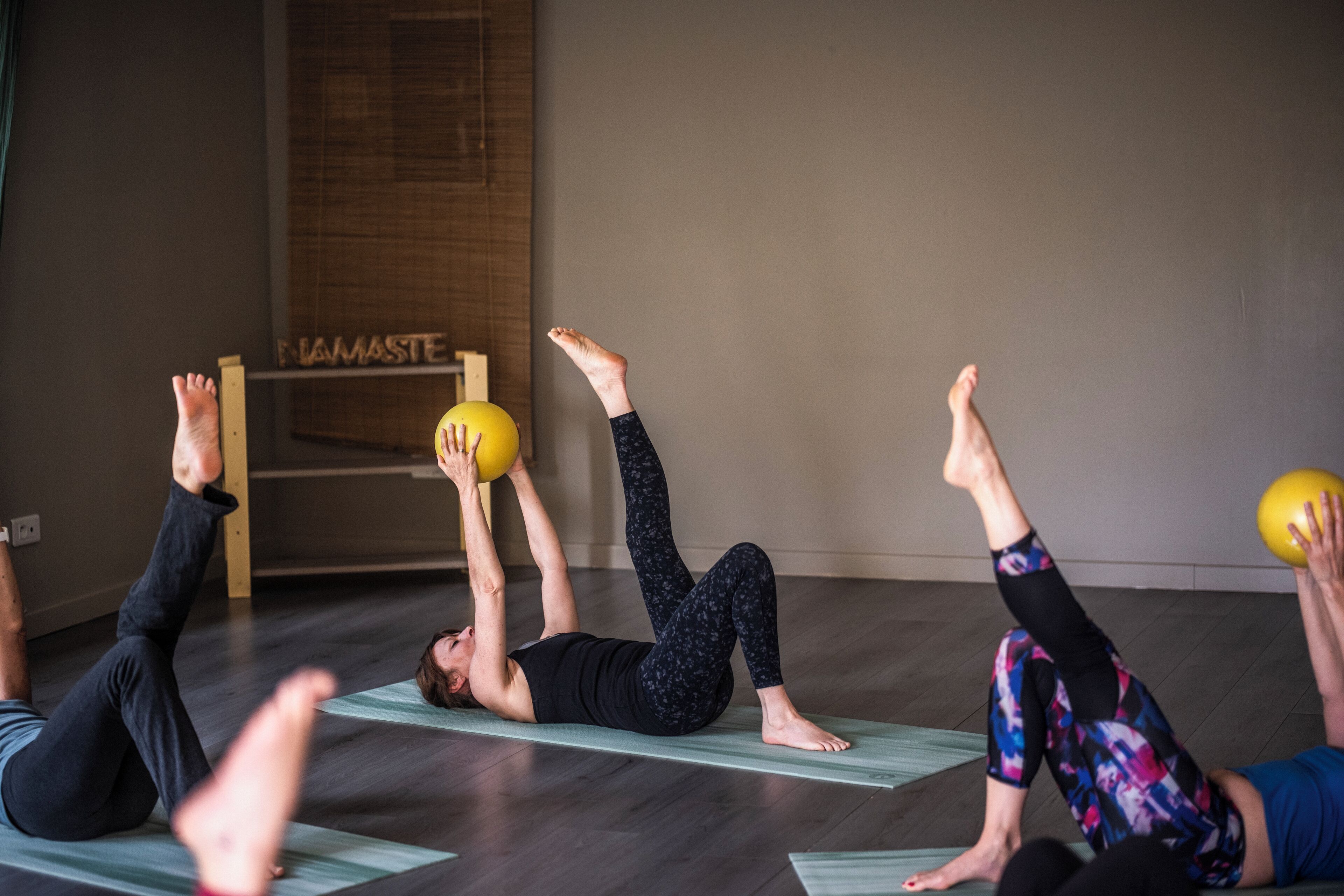 A yoga class in a room with wooden flooring and a sign that reads "PHAMASTE".