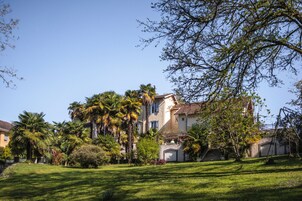 Uma casa grande de dois andares, com gramado bem cuidado e palmeiras.