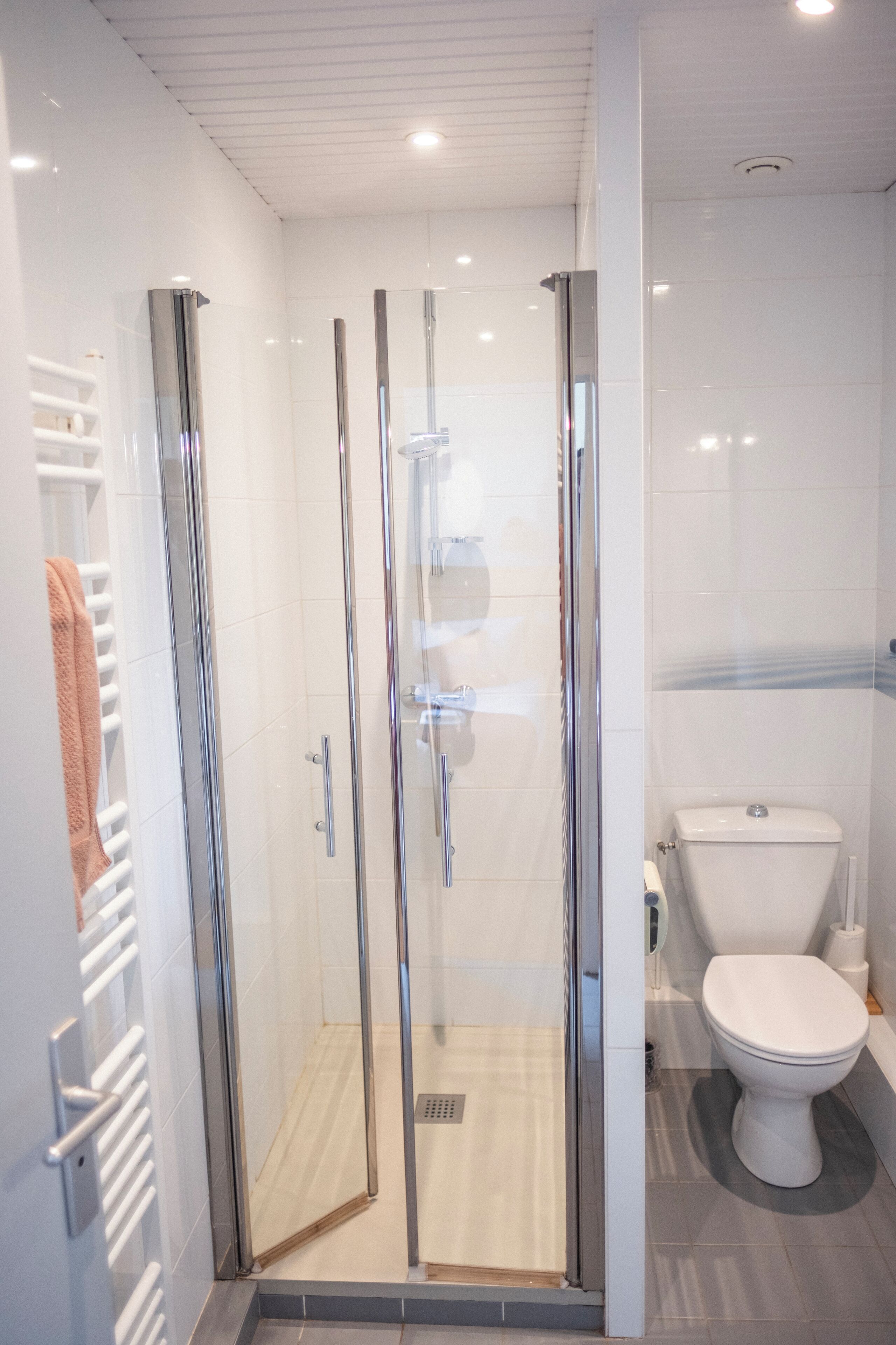 Een moderne badkamer met een douchecabine van glas, een wit toilet en een handdoekrek met een handdoek.