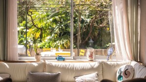 A cozy living room with a sofa, a small table, and a window with a view of greenery. - Maison Tournesol Pau Jurançon Gan (Gan)
