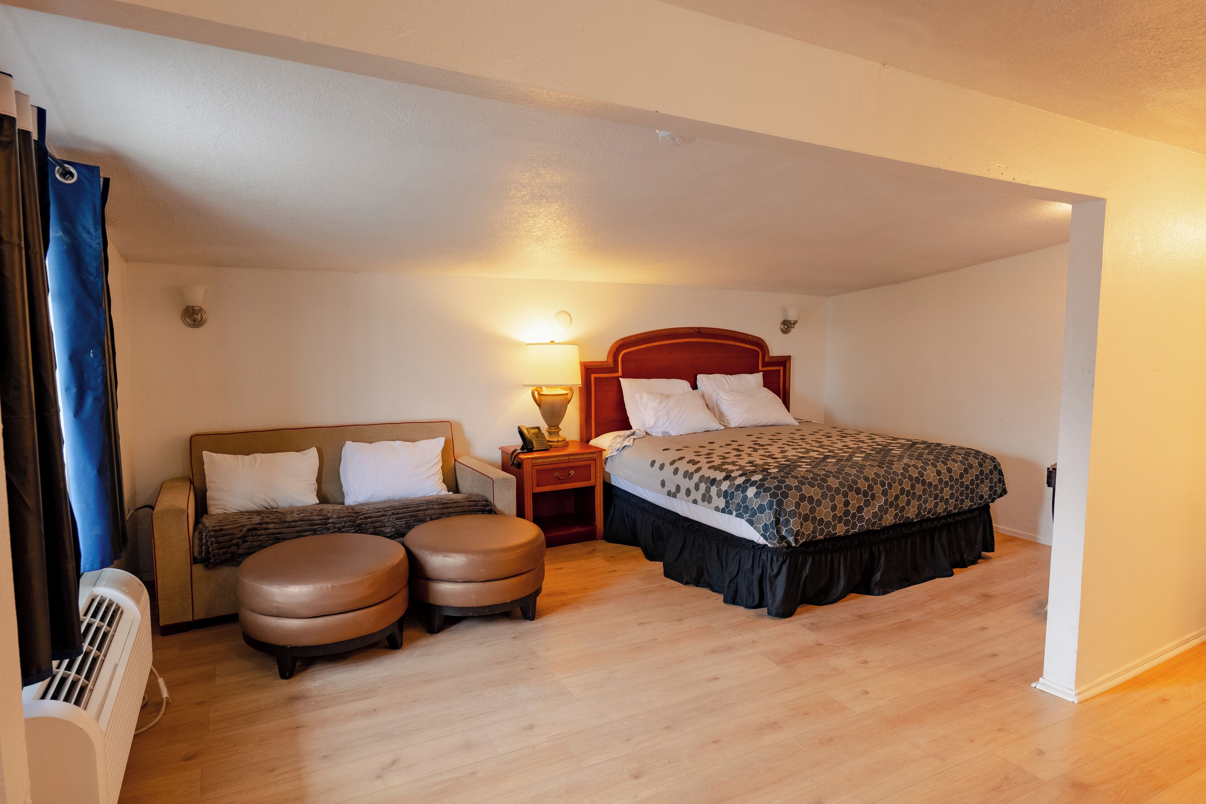 Quarto com cama, sofá, dois pufes, mesa de cabeceira e luminária de parede.