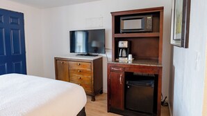 A hotel room with a bed, a wooden dresser, a microwave, and a coffee maker.