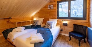Ein gemütliches Schlafzimmer in einer Holzhütte mit zwei Betten, einer Bank und einem Fenster mit Blick auf Bäume.
