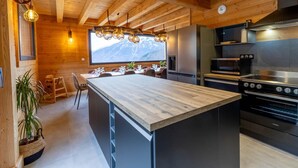 Une cuisine moderne dotée d’un îlot central en bois, d’appareils électroménagers en acier inoxydable et d’une grande fenêtre donnant sur une montagne.