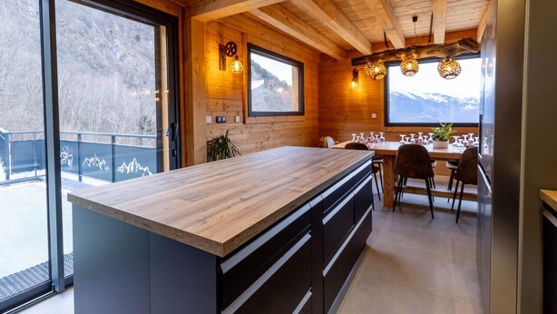 Une cuisine moderne avec des poutres en bois, un grand îlot central et un coin repas offrant une vue sur les montagnes.